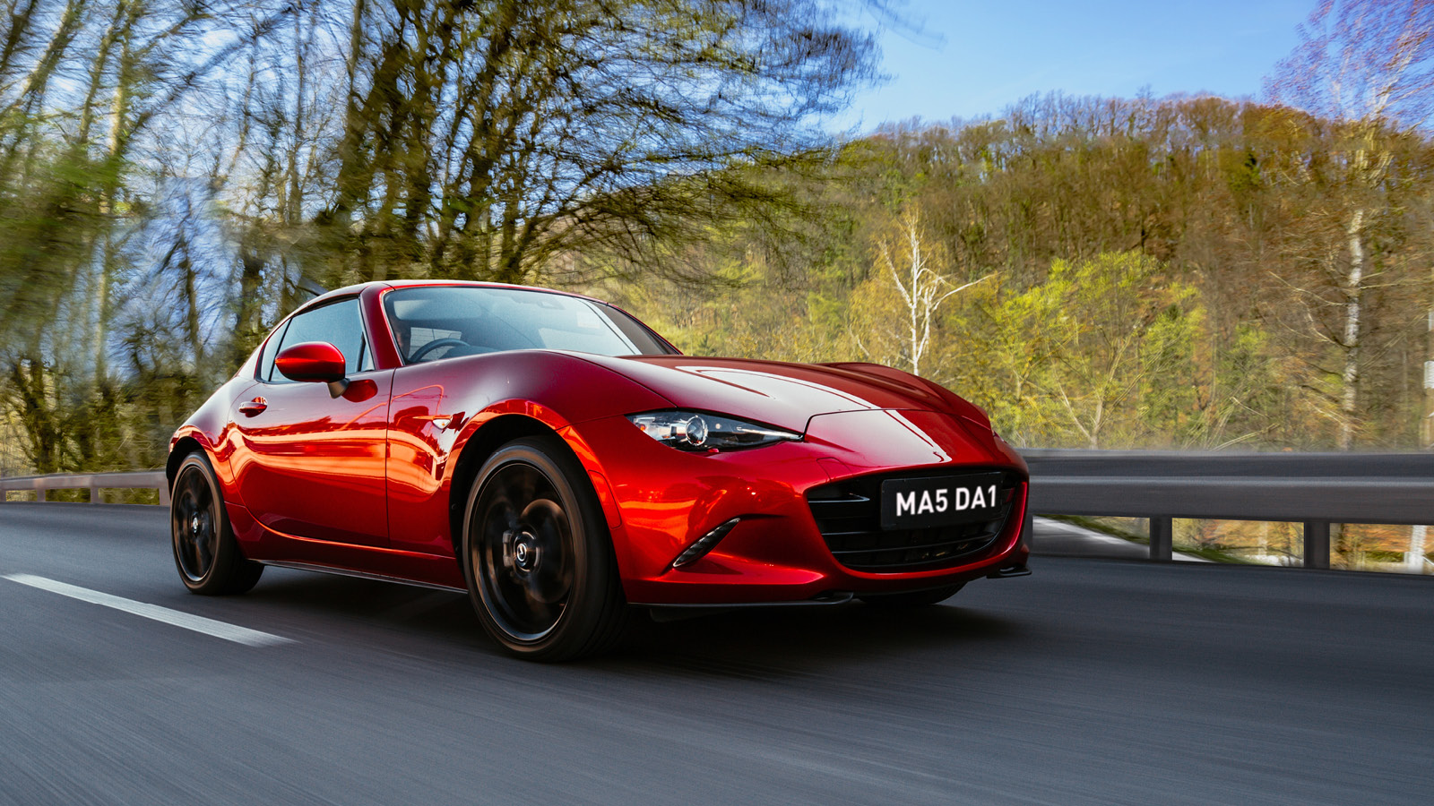 Photo of a red Mazda MX-5 on a road next to the trees