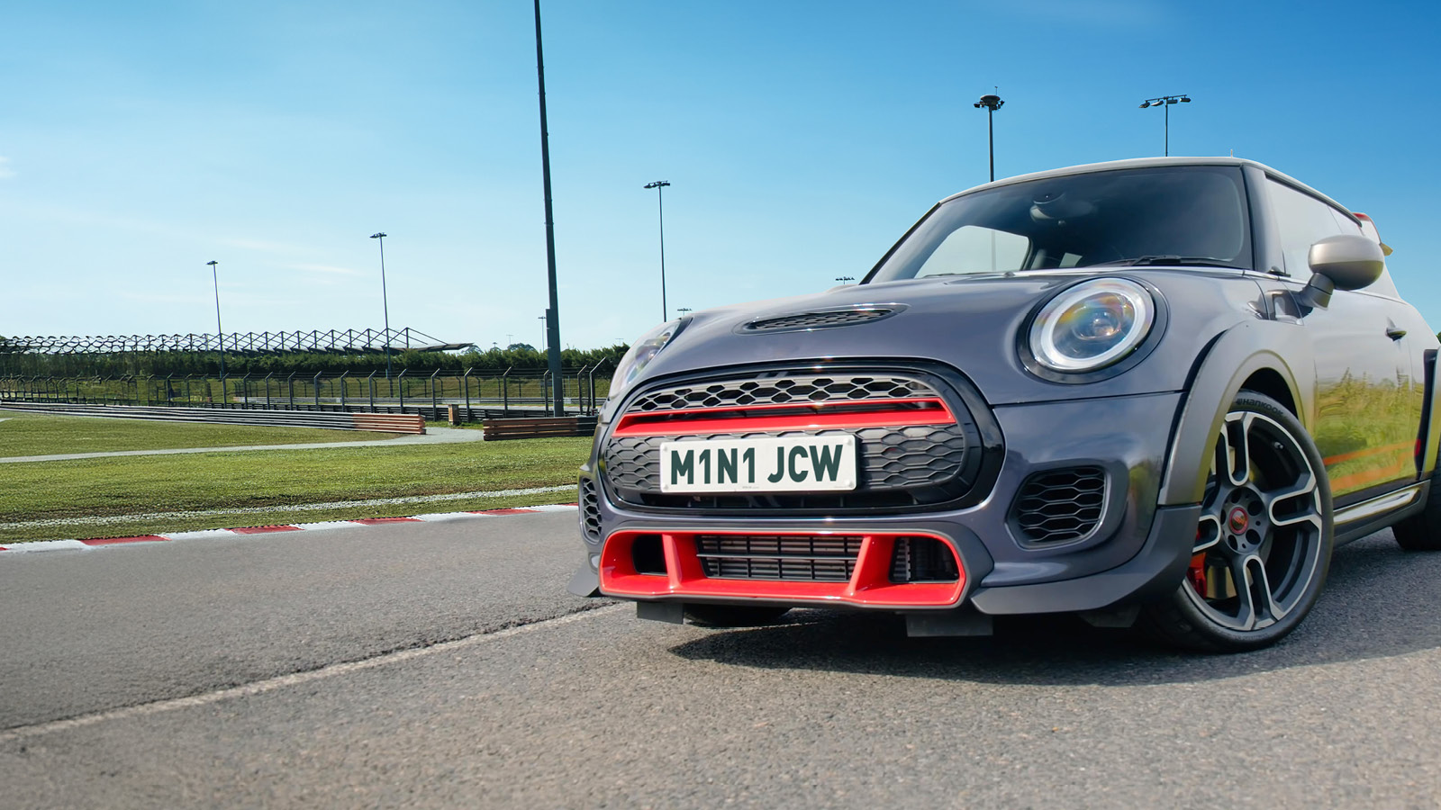 Photo of a grey and red JCW MINI on a race track with a blue sky