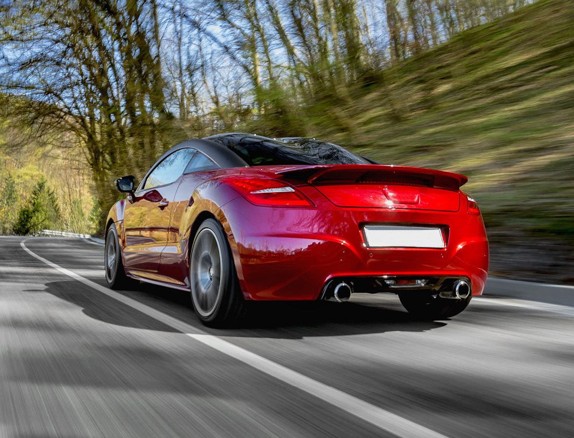 Image of the back of a red car driving on a road with trees at the side